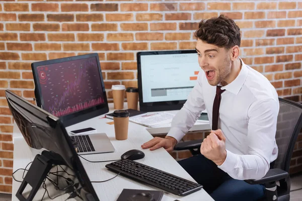 Homme d'affaires excité montrant geste ouais près des ordinateurs et café à emporter dans le bureau — Photo de stock