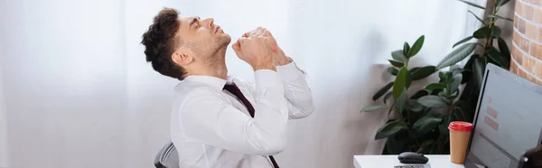 Businessman showing yeah gesture near computer and coffee to go on blurred background, banner — Stock Photo