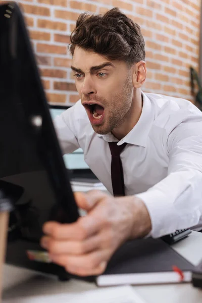 Homem de negócios gritando segurando monitor de computador em primeiro plano desfocado no escritório — Fotografia de Stock