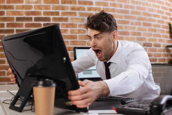 Homem de negócios louco segurando monitor de computador em primeiro plano turvo enquanto verifica o mercado financeiro no escritório — Fotografia de Stock