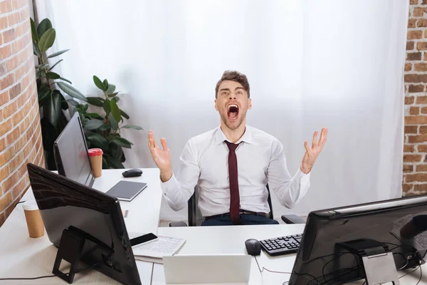 Crazy businessman screaming near devices and newspaper on blurred foreground on table — Stock Photo