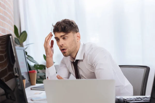 Empresário triste olhando para monitor de computador perto de laptop em primeiro plano desfocado — Fotografia de Stock