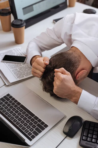 Visão geral do empresário cansado sentado perto de laptop, smartphone e notícias sobre fundo turvo — Fotografia de Stock