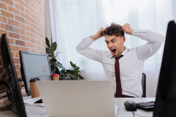 Homem de negócios irritado olhando para computadores enquanto analisa cursos digitais no escritório — Fotografia de Stock