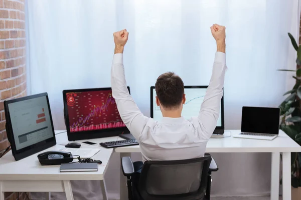 Rückansicht des Geschäftsmannes zeigt yeah Geste in der Nähe von Computern mit Grafiken auf verschwommenem Hintergrund im Büro — Stockfoto