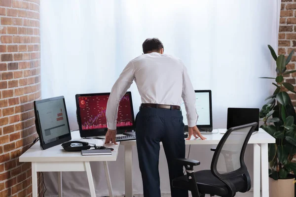 Visão traseira do empresário em pé perto de computadores com gráficos no escritório — Fotografia de Stock