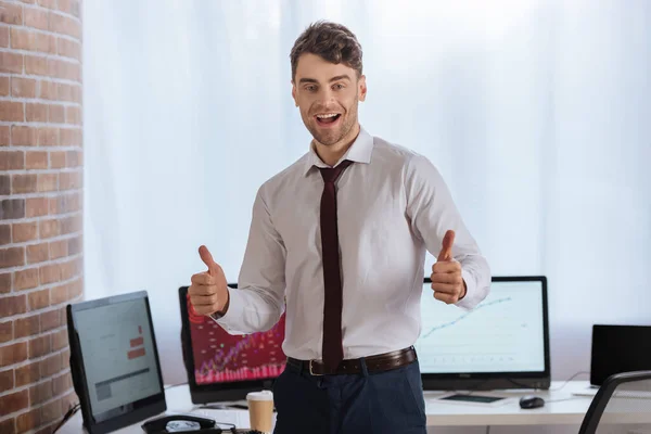 Hombre de negocios alegre mostrando como gesto con computadoras en un fondo borroso - foto de stock