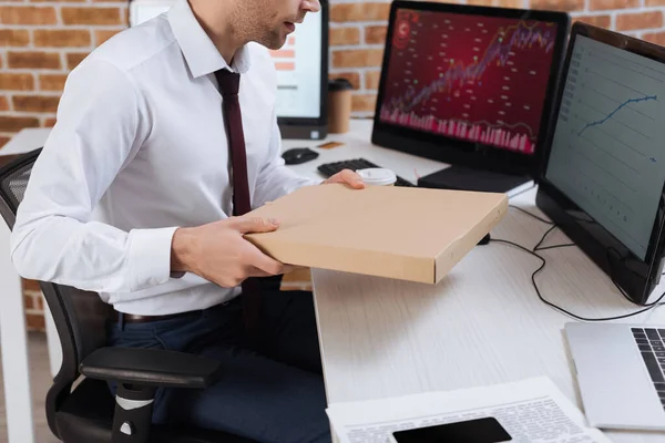 Cropped view of businessman holding pizza box near computers on blurred background in office — Stock Photo