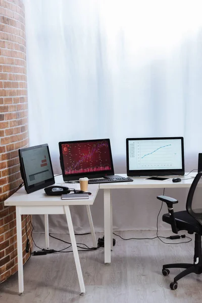 Computers with finance charts on monitors near digital tablet, coffee to go and telephone on table in office — Stock Photo