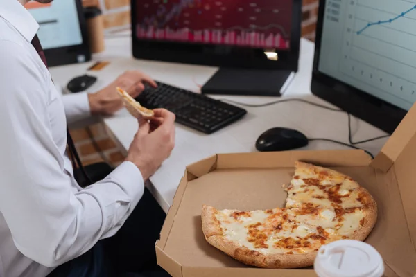 Vue recadrée de pizza savoureuse en boîte près de l'homme d'affaires en utilisant l'ordinateur sur fond flou — Photo de stock