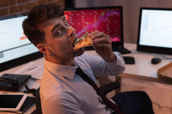 Empresario mirando la cámara mientras come pizza en la oficina por la noche - foto de stock