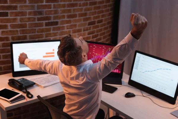 Geschäftsmann dehnt sich in der Nähe von Computern mit Diagrammen auf verschwommenem Hintergrund am Abend — Stockfoto