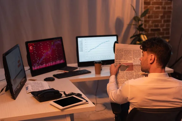Visão traseira do empresário segurando jornal perto de computadores no fundo borrado à noite — Fotografia de Stock