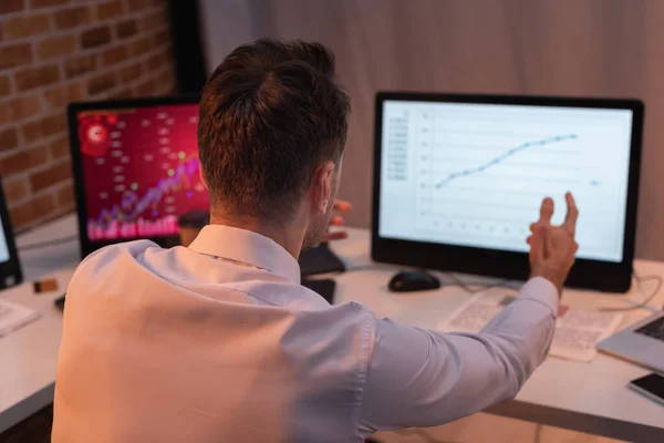 Vue arrière de l'homme d'affaires pointant vers l'ordinateur avec des tableaux financiers sur fond flou — Photo de stock