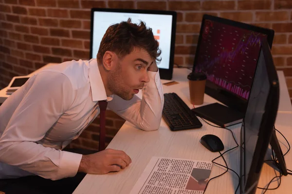 Exhausted businessman looking at computer monitor near newspaper in office during evening — Stock Photo