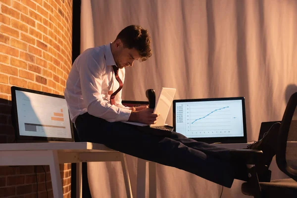 Businessman holding digital tablet and telephone handset near computers in evening — Stock Photo