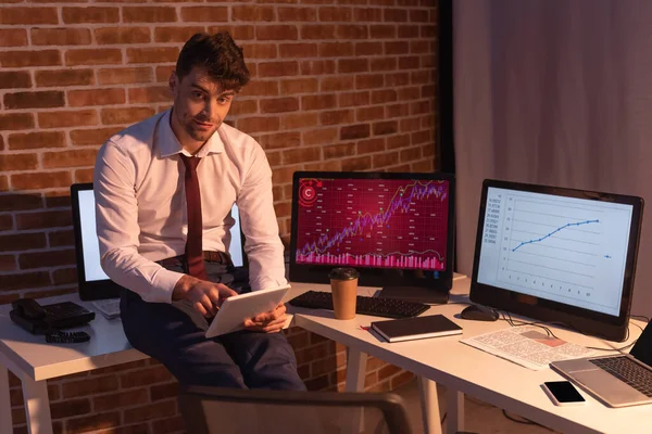 Hombre de negocios usando tableta digital cerca de computadoras, café para llevar y periódico en la oficina - foto de stock