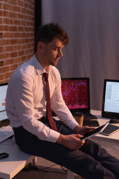 Geschäftsmann hält digitales Tablet in der Nähe von Computern mit Diagrammen auf verschwommenem Hintergrund — Stockfoto