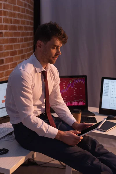 Businessman holding digital tablet near computers with charts on blurred background — Stock Photo