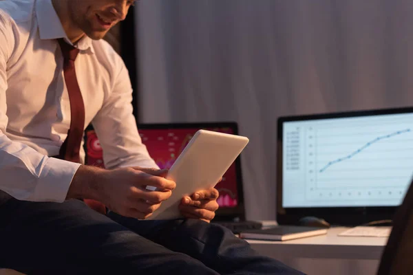 Обрезанный вид цифрового планшета в руках бизнесмена на размытом фоне в офисе вечером — стоковое фото