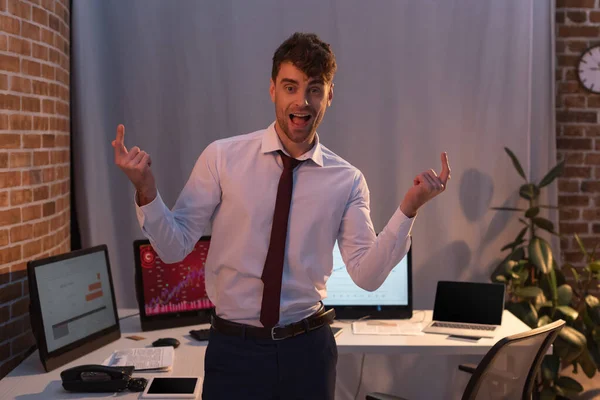 Cheerful businessman pointing with fingers near computers on blurred background — Stock Photo