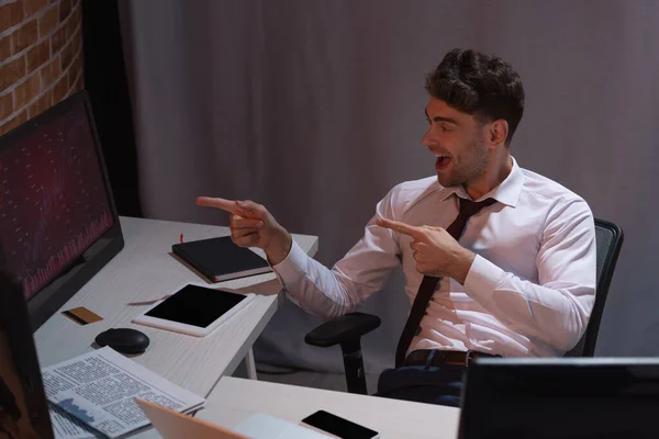 Smiling businessman pointing at computer near newspaper and devices in office — Stock Photo