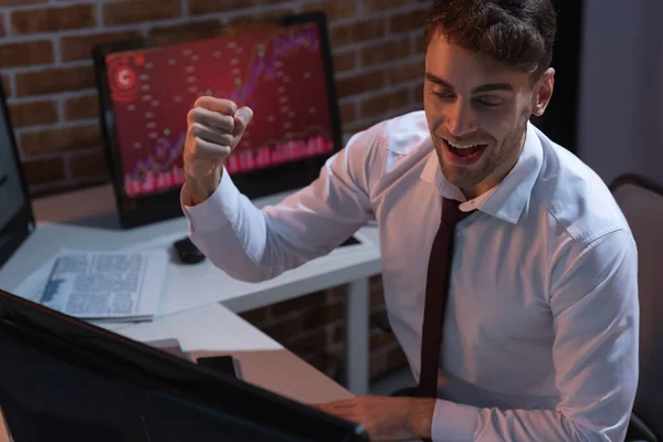 Businessman showing yeah gesture near computer on blurred foreground in evening — Stock Photo