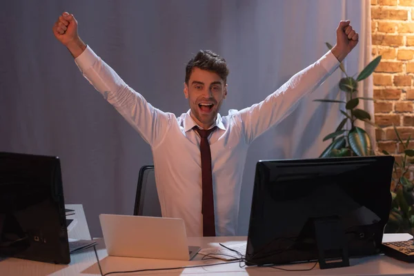 Positive businessman showing yeah gesture near devices in evening — Stock Photo