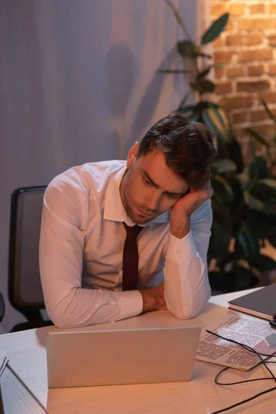 Trauriger Geschäftsmann blickt abends auf Laptop neben Zeitung — Stockfoto
