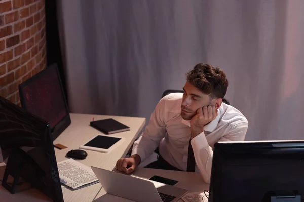 Businessman looking at computer near laptop, smartphone and newspaper in office — Stock Photo