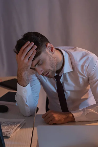 Müder Geschäftsmann sitzt im Büro neben Geräten und Zeitung im verschwommenen Vordergrund — Stockfoto