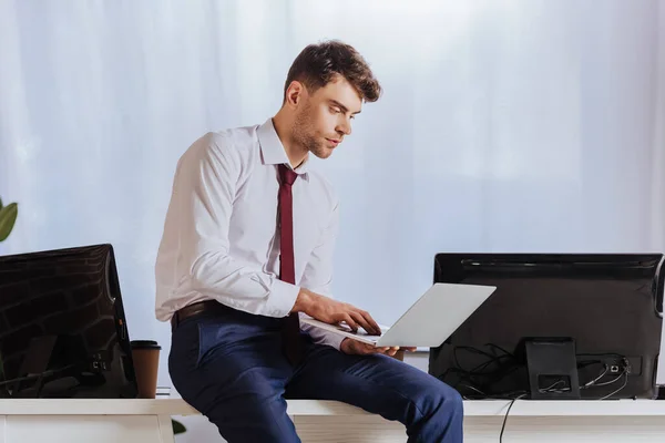 Jeune homme d'affaires utilisant un ordinateur portable près des ordinateurs et du café pour aller au bureau — Photo de stock