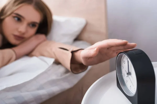 Jovem mulher atingindo despertador na mesa de cabeceira — Fotografia de Stock