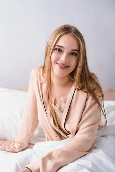 Freudige junge Frau in Seidenmantel lächelt im Schlafzimmer — Stockfoto