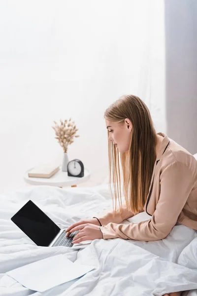 Joven freelancer en bata de seda usando portátil con pantalla en blanco en el dormitorio - foto de stock