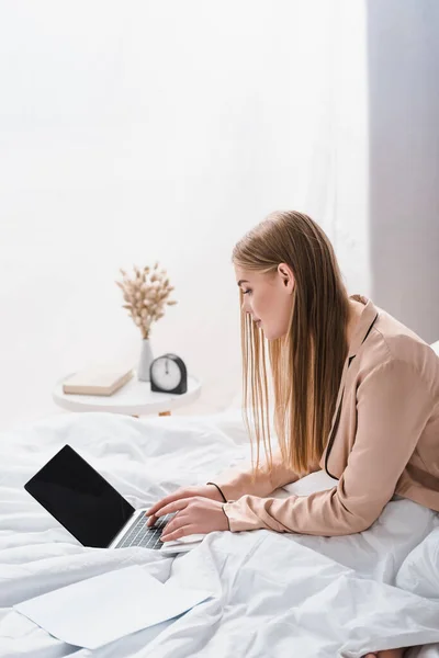 Young freelancer in silk robe using laptop with blank screen in bedroom — Stock Photo