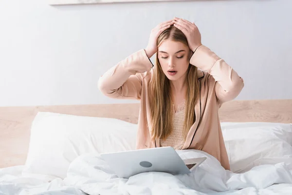Jovem freelancer chocado em robe de seda olhando para laptop no quarto — Fotografia de Stock
