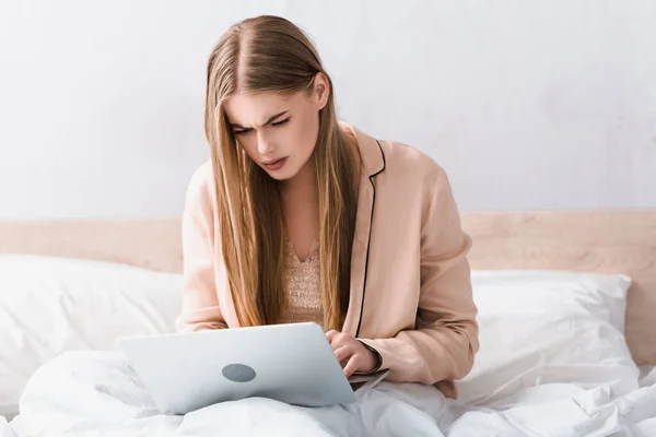 Joven freelancer enfocado en bata de seda usando laptop en el dormitorio - foto de stock