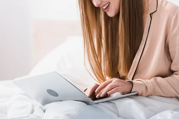 Vista recortada de joven freelancer sonriente en bata de seda usando el ordenador portátil en el dormitorio - foto de stock