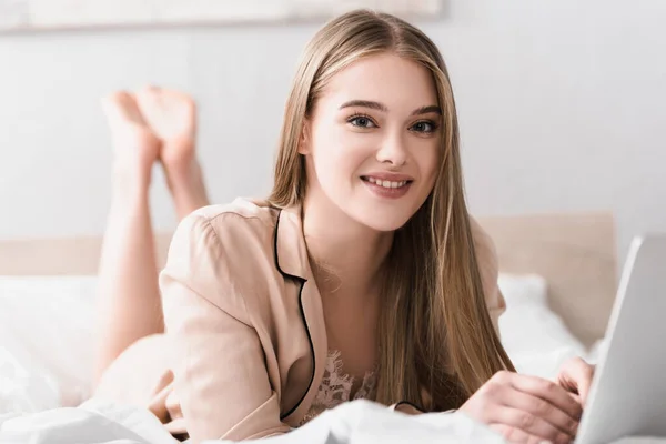 Fröhliche junge Frau, die auf dem Bett liegt und in die Kamera blickt — Stockfoto