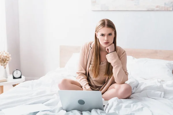 Mulher descontente olhando para a câmera perto do laptop na cama — Fotografia de Stock