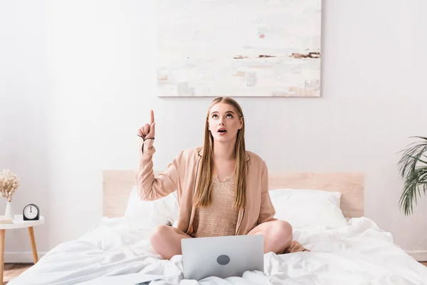 Surprised young freelancer in silk robe having idea near laptop on bed — Stock Photo