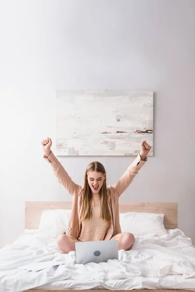 Excited woman with clenched fists looking at laptop on bed — Stock Photo