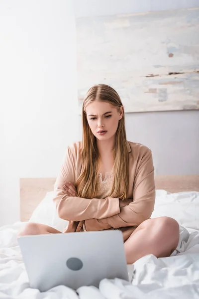 Jeune femme assise avec les bras croisés et regardant ordinateur portable sur le lit — Photo de stock