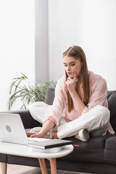 Thoughtful freelancer sitting on couch and using laptop — Stock Photo