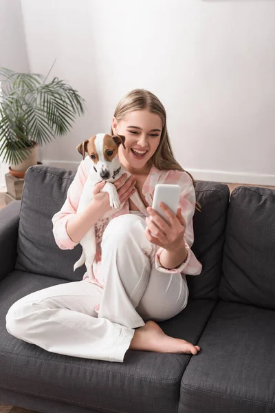 Jovem mulher alegre tomando selfie com jack russell terrier na sala de estar — Fotografia de Stock