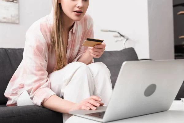 Cropped view of young woman holding credit card and using laptop on coffee table — Stock Photo