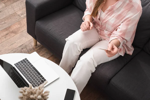 Vue recadrée de la jeune femme tenant carte de crédit près de gadgets sur la table basse — Photo de stock