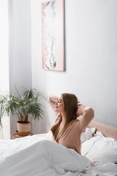 Wache und fröhliche Frau im seidenen Pyjama, die sich im Bett ausstreckt — Stockfoto