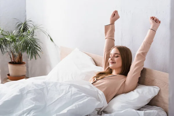Прокинулася і радісна жінка в атласному піжамі, що розтягується в ліжку — стокове фото